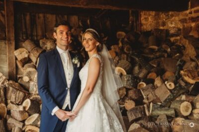 Bride and groom smiling by woodpile.