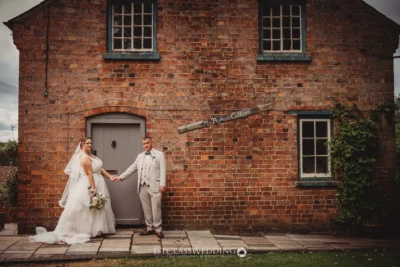 Bride and groom holding hands outside historic brick cottage.