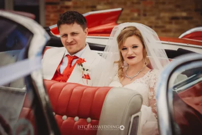 Bride and groom smiling in classic car.