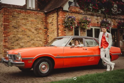 Bride and groom with vintage red car at wedding.