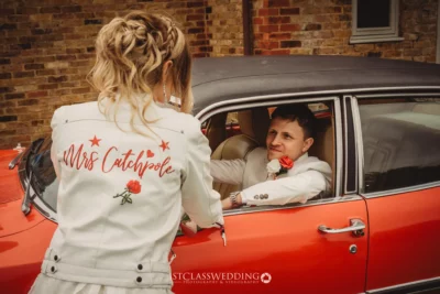 Bride in custom jacket by vintage car with groom.