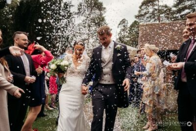 Bride and groom walking under confetti shower at wedding.