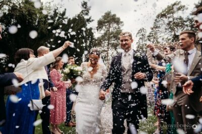 Bride and groom walking through confetti shower outdoors.