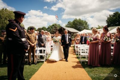 Bride walking down aisle at outdoor military wedding ceremony.