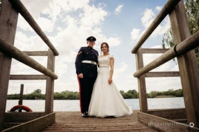 Military groom and bride posing on wooden dock.