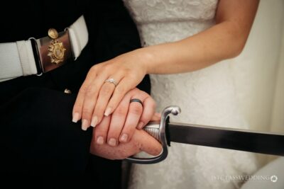 Bride and groom holding hands over sword at wedding.