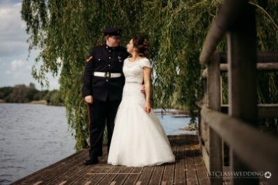 Bride and groom in uniform by lakeside.