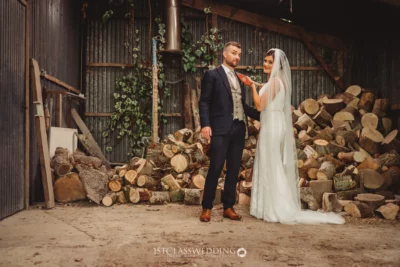 Couple posing at rustic wedding, woodpile backdrop.