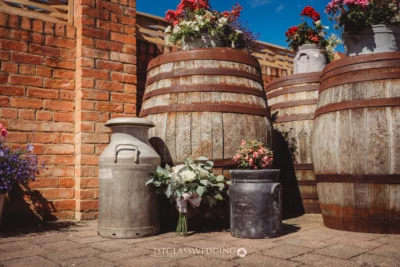Rustic wedding bouquet beside vintage barrels and milk churns.