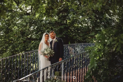 Bride and groom smiling on bridge, nature background.