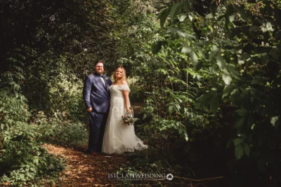 Couple posing in sunlit forest on wedding day.
