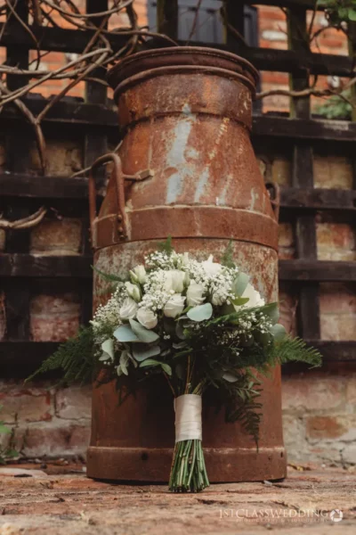 Rustic milk churn with bridal bouquet outdoors.