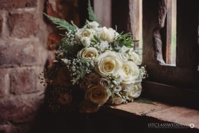 Elegant white wedding bouquet near rustic window.