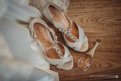 Elegant bridal shoes and perfume on wooden floor.