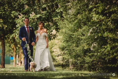 Bride, groom, and dog walking in park at wedding.