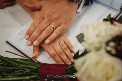 Newlywed hands with wedding rings on marriage certificate.