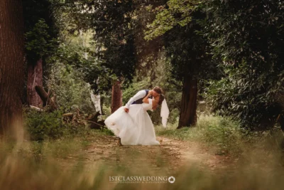 Bride and groom kissing in forest pathway.