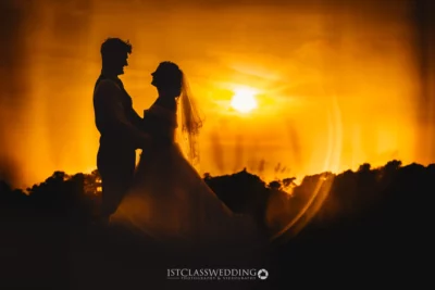 Couple silhouette against sunset at wedding.