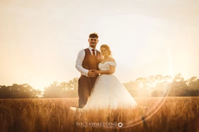 Couple embracing in sunset-lit field on wedding day.