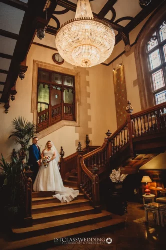 Couple on staircase under chandelier in historic venue.