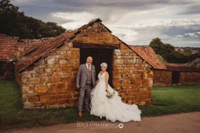 Bride and groom posing by rustic stone building.