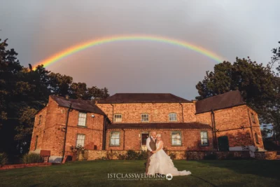 Wedding couple posing under rainbow at brick venue.