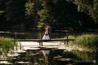 Couple kissing on bridge by serene lake.