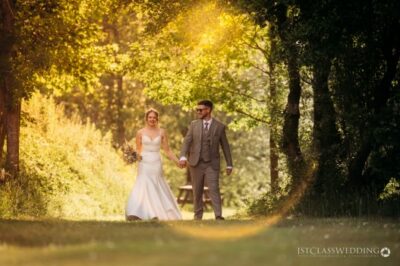 Couple walking hand in hand in sunlit woodland.