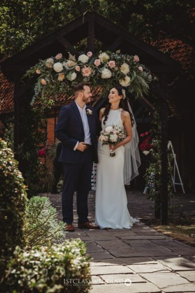 Couple smiling under floral archway at wedding.