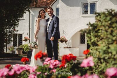 Wedding couple posing by white historic building with flowers.