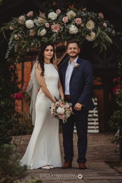 Bride and groom posing under floral archway at wedding.