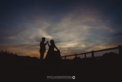 Silhouetted couple against sunset sky.