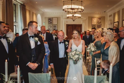 Bride walking aisle with father at elegant wedding ceremony.
