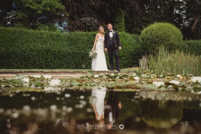 Couple by lily pond in wedding attire.