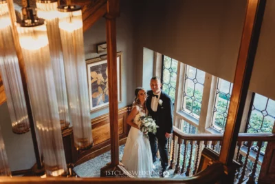 Bride and groom posing on elegant wooden staircase.