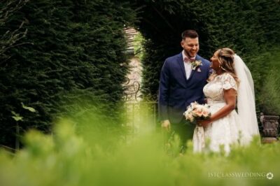 Bride and groom smiling in garden aisle.