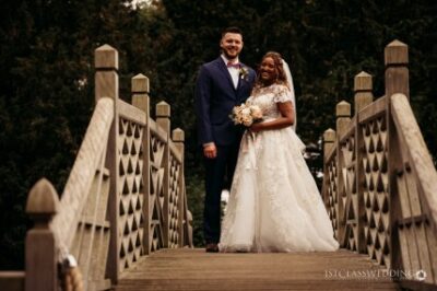 Bride and groom smiling on wooden bridge outdoors.