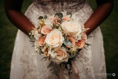 Bride holding peach rose bouquet at wedding.