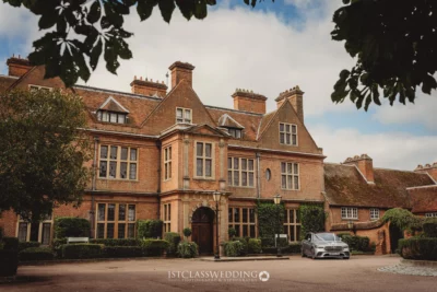 Elegant British manor with landscaped entrance and parked car.