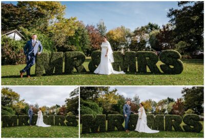 Bride and groom posing by 'MR & MRS' hedge.