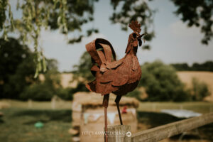 Rustic metal rooster sculpture in countryside setting.