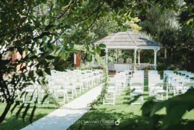 Outdoor garden wedding setup with white chairs and gazebo.