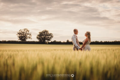 Couple holding hands in wheat field at sunset