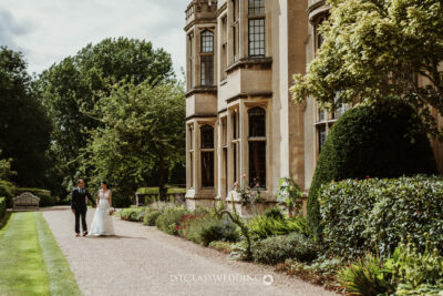 Bride and groom walking by historic manor house garden.