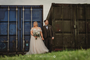 Bride and groom posing by industrial containers.