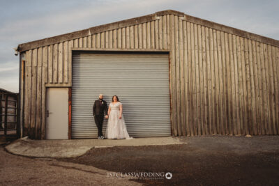 Couple posing by industrial warehouse for wedding photo.