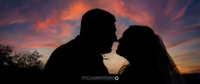 Silhouetted couple kissing against sunset sky.