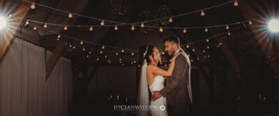 Couple embracing under twinkling lights at wedding venue.