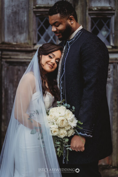 Interracial couple posing in wedding attire with bouquet.