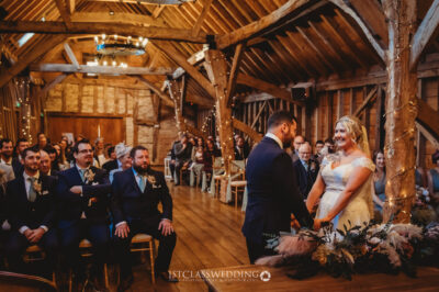 Rustic barn wedding ceremony with smiling bride and groom.